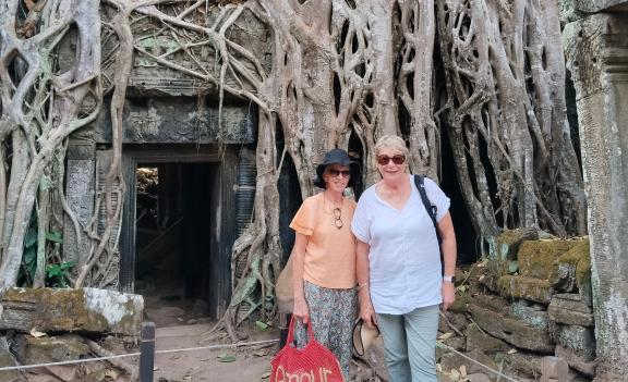 Diane and Colleen standing beside ancient tree roots at Ta Prohm temple in Siem Reap